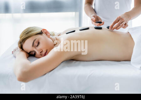 cropped view of masseur doing hot stone massage to woman in spa Stock Photo