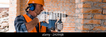 panoramic shot of handsome bearded man using hammer drill near brick wall Stock Photo