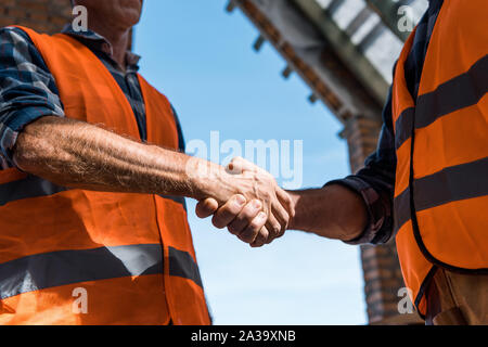 cropped view of men shaking hands against blue sky Stock Photo