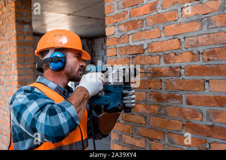 handsome constructor in helmet holding hammer drill Stock Photo