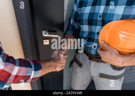 cropped view of builders shaking hands while standing near door Stock Photo