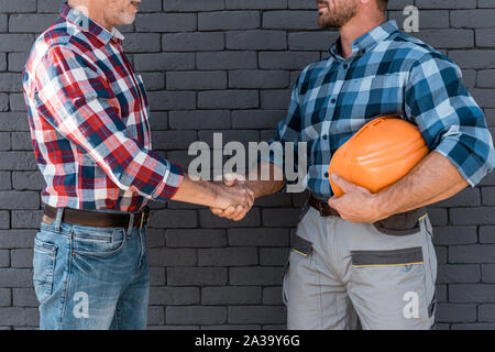 cropped view of men shaking hands while standing near brick wall Stock Photo