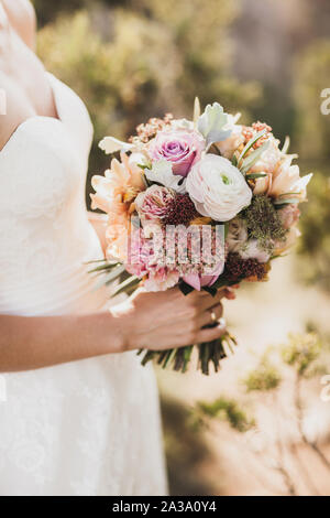 Bride holding in hands small wedding bouquet in orange autumn colors. Pink and orange roses, white peony, dried flowers and leaves. Stock Photo