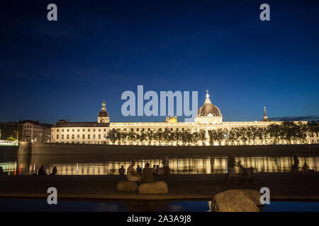 LYON, FRANCE - JULY 18, 2019: French people sitting on the riverbank of the Quais De Rhone, facing Hotel Dieu, one of the main monuments of the city f Stock Photo