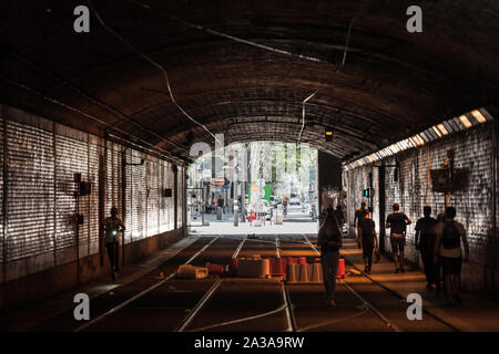 LYON, FRANCE - JULY 14, 2019: People walking in a dark tunnel towards the end, made of light colors, in an underground tram passage, during a sunny af Stock Photo