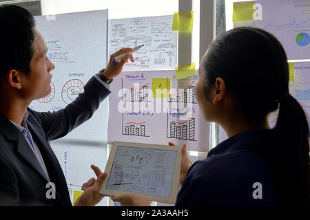 Business people holding tablet computer with ideas for new business and discussing pie chart hanging on glass wall in office building Stock Photo