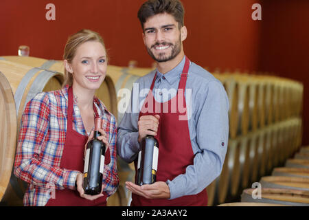 young couple showing their bottled red wine in cellar Stock Photo
