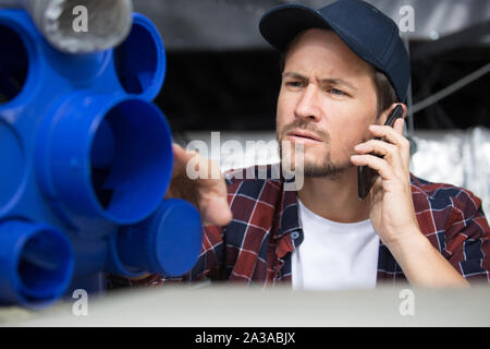 young repairman contractor on the phone repairing heating panel Stock Photo
