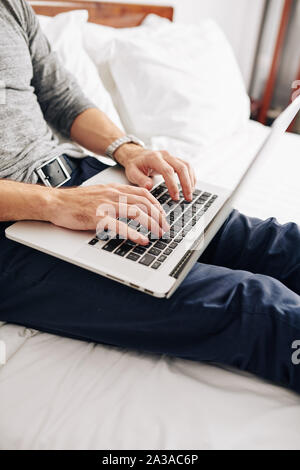 Cropped image of coding young man sitting on bed. Programmer working from home Stock Photo