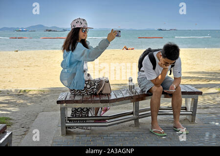 Woman taking selfie photograph with her smartphone whilst her boyfriend is preoccupied with his smartphone. Modern couples Stock Photo