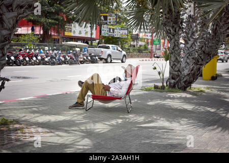 Man sitting in a folding chair recliner on the pavement at Pattaya Thailand Stock Photo