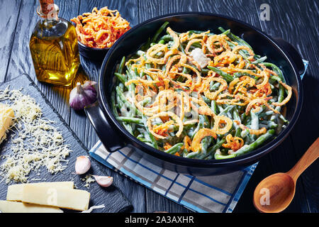 Homemade Green Bean Casserole topped with French crispy fried onions in a black dish on a black wooden table, close-up Stock Photo