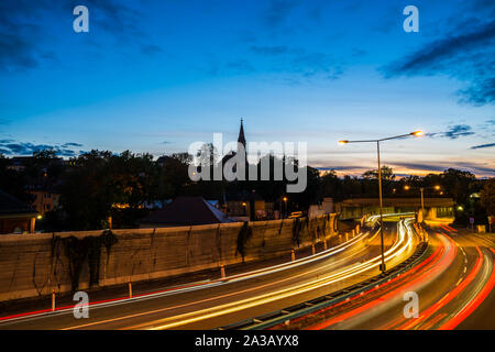 Germany, Beautiful sunset sky over ancient beger church in stuttgart district berg, behind light trails of driving cars on highway Stock Photo