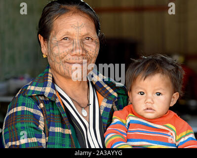 Elderly Chin Muun tribal woman ('spider woman') with traditional facial tattoo smiles for the camera together with her cute little grandson. Stock Photo