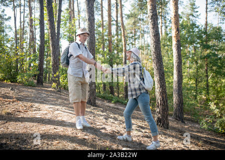 Couple of mature adults wearing backpacks walking in forest Stock Photo