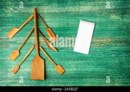 Flat lay background. Christmas tree made of kitchen utelits on old wooden table with notepad and copys pace for text. Stock Photo