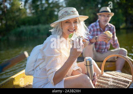 Beautiful wife eating sandwich while sitting in boat with husband Stock Photo