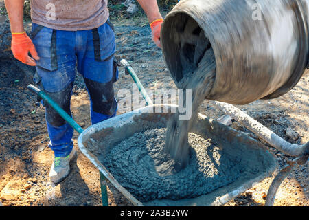 Builder pouring cement from a cement mixer into a wheelbarrow waiting as it fills in a building and construction concept Stock Photo