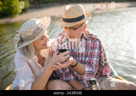 Wife wearing summer hat giving some tea to her husband Stock Photo