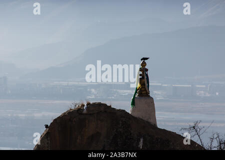 A bird perches on top of a shrine at the Drepung Buddhist Monastery near Lhasa, Tibet.  In the background are the mountains and the suburbs of Lhasa. Stock Photo