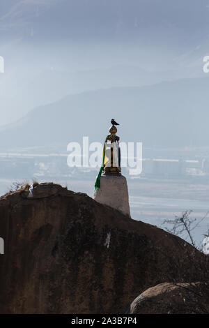 A bird perches on top of a shrine at the Drepung Buddhist Monastery near Lhasa, Tibet.  In the background are the mountains and the suburbs of Lhasa. Stock Photo