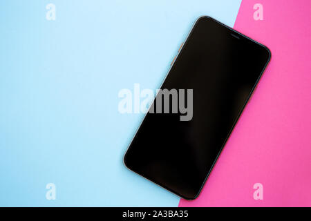 Smartphone with empty black screen in flat lay on light blue & pink background.Big modern mobile phone with blank touchsreen panel.Place application l Stock Photo