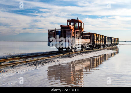 Awesome train rides on the rail in the water with white salt on the background of beautiful blue sky. Stock Photo