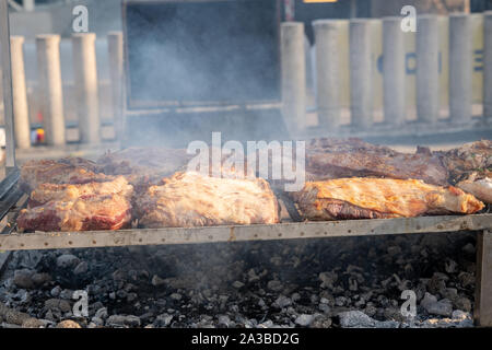 BBQ beef lined up on a large outdoor grill with smoke coming up from the fire below. Stock Photo