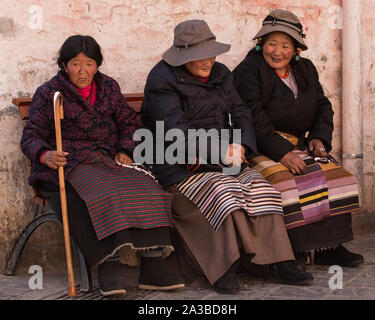 Three Tibetan women pilgrims in traditional dress take a break while circumambulating the Jokhang Temple in Lhasa, Tibet.  Wearing pangden aprons. Stock Photo