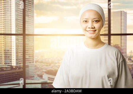 Asian woman in a white shirt with a smile on her face standing with cityscapes background. Cancer awareness Stock Photo
