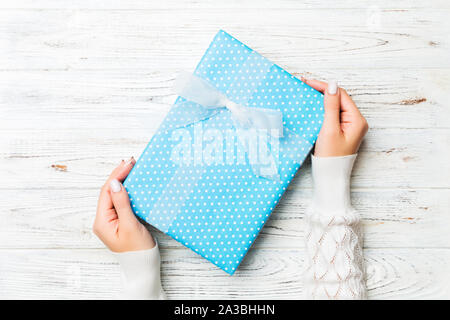 Woman arms holding gift box with colored ribbon on white rustic wooden table background, top view and copy space for you design. Stock Photo
