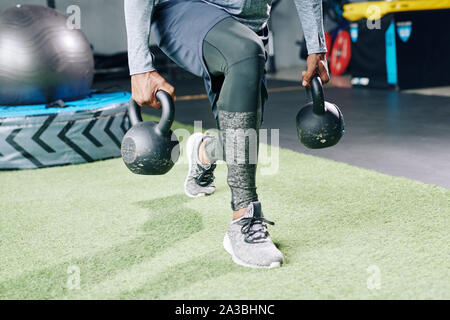 Close-up image of fit strong man doing deep lunges with heavy kettlebessl in both hands Stock Photo