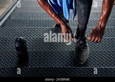 Close-up image of sweaty sportsman standing on steps and tying shoe laces when resting between sets Stock Photo
