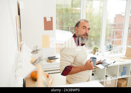 High angle portrait of bearded senior man drinking morning coffee in kitchen and looking up at camera, copy space Stock Photo