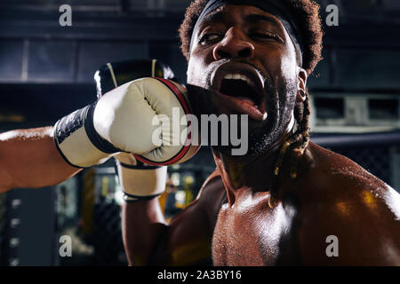 Close-up image of boxer getting punch to the jaw during match in boxing cage Stock Photo