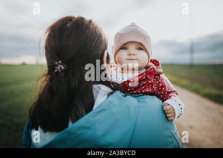 Infant baby looks over mothers shoulder - autumn outdoor family lifestyle concept Stock Photo