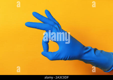 Hand in a blue protective glove on a yellow background. Fingers showing OK sign. Stock Photo