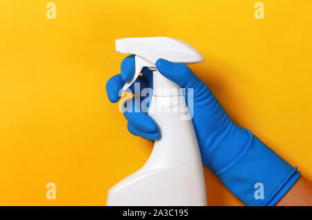 Worker's hand in a rubber blue protective glove with a spray gun on a yellow background. The concept of cleaning, home care. Stock Photo