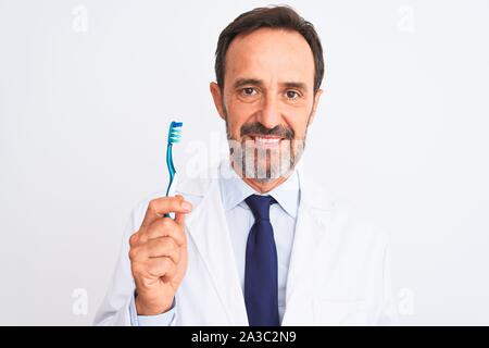 Middle age dentist man holding toothbrush standing over isolated white background with a confident expression on smart face thinking serious Stock Photo