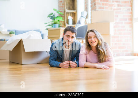 Young beautiful couple in love relaxing lying on the floor together with cardboard boxes around for moving to a new house Stock Photo