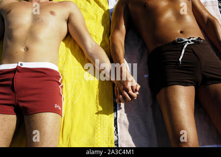 two men lying on the beach hand in hand Stock Photo