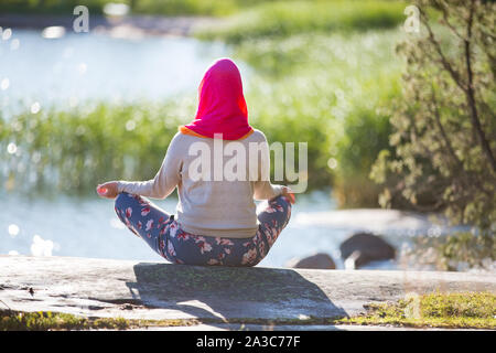 Attractive woman in hijab training in the park, meditating. Doing yoga exercises on fresh air and enjoying early morning. Healthy lifestyle Stock Photo
