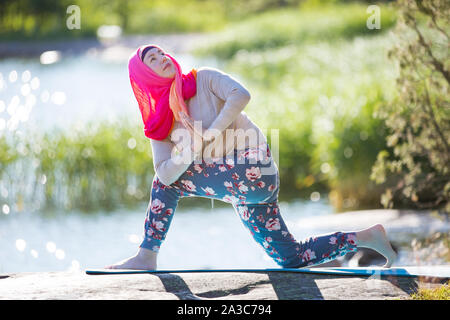 Attractive woman in hijab training in the park, meditating. Doing yoga exercises on fresh air and enjoying early morning. Healthy lifestyle Stock Photo