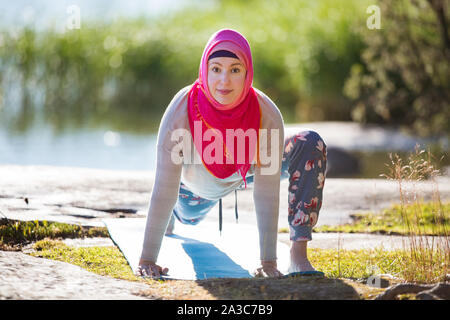 Attractive woman in hijab training in the park, meditating. Doing yoga exercises on fresh air and enjoying early morning. Healthy lifestyle Stock Photo