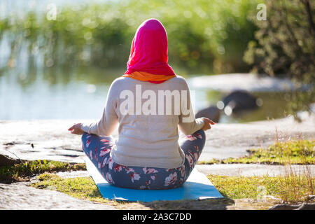 Attractive woman in hijab training in the park, meditating. Doing yoga exercises on fresh air and enjoying early morning. Healthy lifestyle Stock Photo