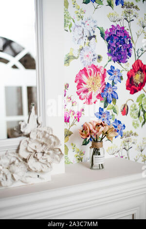 Bright vertical interior with colored wallpaper. A bouquet of flowers stands in a vase on a white fireplace. Beautiful interior of an expensive room. Stock Photo