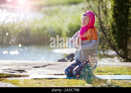 Attractive woman in hijab training in the park, meditating. Doing yoga exercises on fresh air and enjoying early morning. Healthy lifestyle Stock Photo