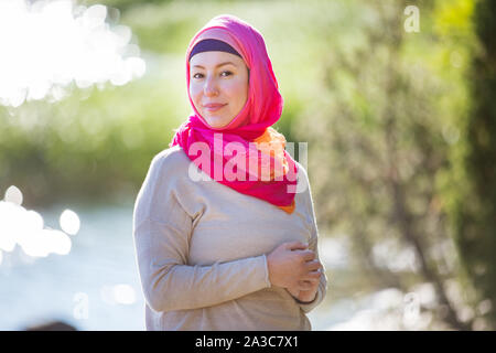 Attractive confident woman in hijab standing outdoors in sunny summer day, happily smiling. Muslim woman lifestyle concept Stock Photo