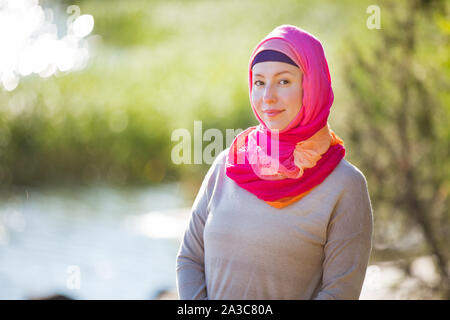 Attractive confident woman in hijab standing outdoors in sunny summer day, happily smiling. Muslim woman lifestyle concept Stock Photo