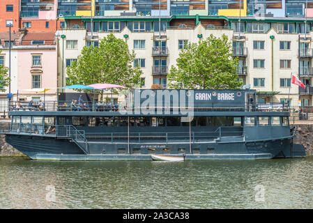 Seen along the Harbourside in Bristol UK. Grain Barge is a floating Pub, one of the Guardian Papers top 50 with the colourful houses of Clifton Wood. Stock Photo
